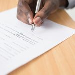 A person filling out a court record form by hand while seated at a desk